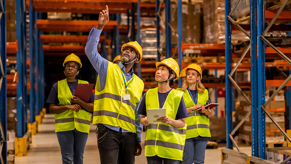 A Warehouse Manager Guiding A Diverse Team During An Inspection